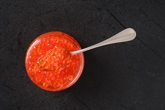 Overhead view of open jar with red caviar and a spoon in it