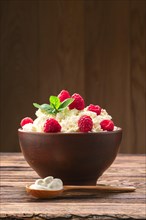 Wooden spoon with sour cream near clay plate with fresh cottage cheese with raspberries and mint
