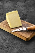 Triangular piece of hard cheese on wooden cutting board
