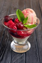 A cup of cherry ice cream decorated with raspberries and dewberry and mint leaves