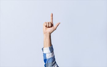 Hand gesturing the letter L in sign language on an isolated background. Man's hand gesturing the letter L of the alphabet isolated. Letters of the alphabet in sign language