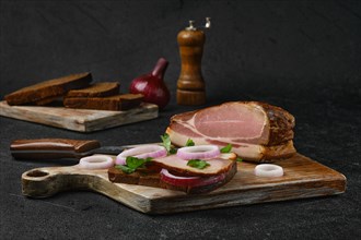 Rural sandwich with smoked bacon with brown bread on wooden cutting board