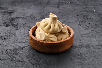 Uncooked khinkali in wooden plate on black wooden background