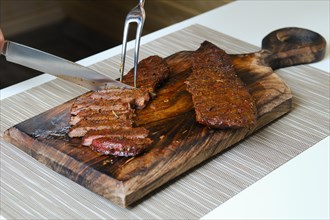 Cutting grilled steak on wooden cutting board with knife and fork