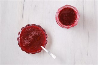Top view of jar and saucer with cherry jam on white wooden background