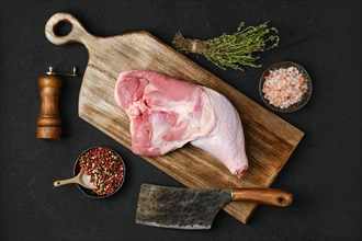 Overhead view of raw turkey leg with skin on cutting board with cooking ingredients on black background