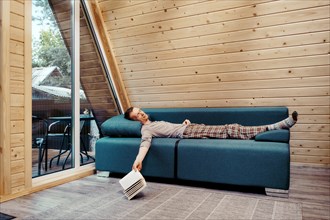 Middle-aged man peacefully napping on the sofa in his country house. He dropped the book on the floor