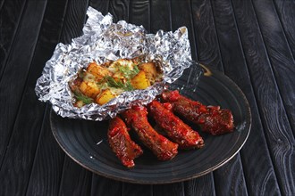 Fried spicy ribs with potato baked with cheese in foil