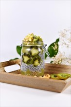 Green fruit smoothie layered in glass with chia seed pudding topped with star shaped banana and kiwi slices on wooden tray