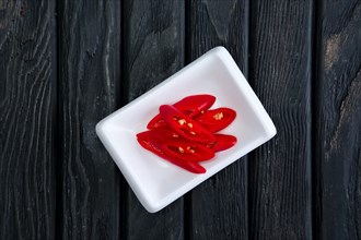 Pieces of chilli in plate on dark wooden background. Top view