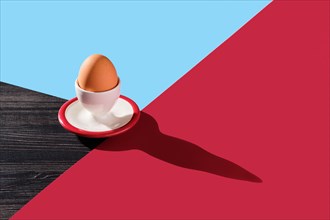 Egg cup with brown egg on abstract colorful background and long shadow