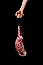 Hand of a butcher holds raw leg of lamb over black background