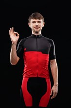 Sport. Cyclist in training clothes on black background shows OK sign