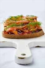 Closeup view of salmon sandwich with caramelized onion on wooden serving board