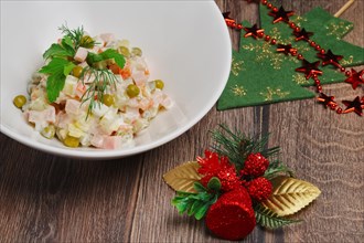 Russian traditional salad olivier with pea on wooden table near new years decorations