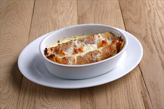 Fried pancakes stuffed with ham and covered with melted cheese on wooden table