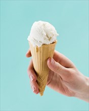 Hand holding vanilla ice cream cone blue background