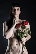 Naked young woman with tattoos and red roses