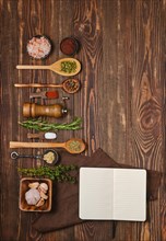 Top view of open notepad for recipes next to kitchen spoons and bowls with various spices