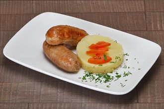 Plate with fried small sausage with mashed potato and cabbage on wooden table