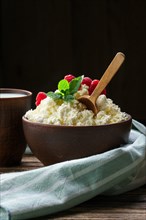 Fresh cottage cheese with raspberries and wooden spoon in clayware on wooden table