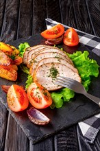 Sliced baked ham with fresh tomatoes on a stone plate in a rustic style