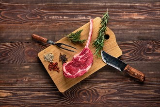 Overhead view of raw cowboy steak on wooden cutting board with spice