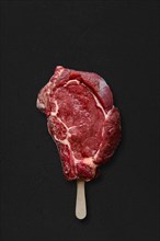 Raw beef rib steak with ice-cream stick on black background