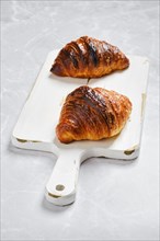 Fresh croissant for breakfast on wooden serving board on marble background