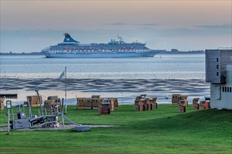 Grassy beach with beach chairs and cruise ship Artania on the Weser at dusk