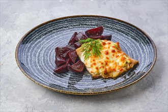 Fried cod fillet with melted cheese topping and roasted beetroot slices on grsy stone background