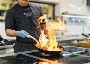 Chef with apron gloves flambeing dish