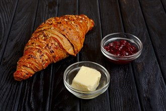 Croissant with jam and butter on dark wooden table