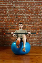 Athletic man doing exercises for the balance on rubber ball with gymnastic Athletic man doing balancing exercises over the gym ball with gymnastic stick