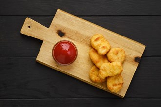 Top view of crispy chicken nuggets in breading served with ketchup on wooden board