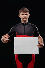 Sport. Cyclist in training clothes on black background holding blank sheet of paper. Your text here