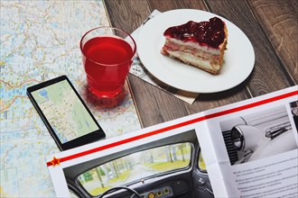 Cup of fruit-drink near map and smartphone with magazine on the table. Top point of view