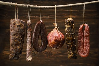 Assortment of dried meat and sausages hanging on a stick in a barn