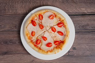 Pizza with ham and tomato on wooden table