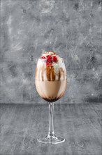 Glass of cold coffee drink with whipped cream and cherry in shabby gray background