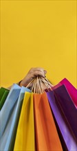 Close-up of a woman's hand holding colorful shopping bags over yellow background