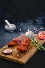Smoky skewers with marinated raw pork meat on dark background