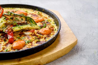 Closeup view of eggs with bell pepper and zucchini baked in oven in cast-iron skillet