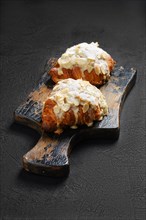 Two crispy croissant with caramel and peanut shavings on wooden serving board