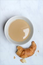 Coffee with milk in bowl and croissant