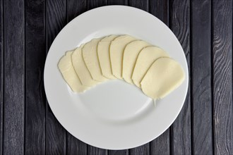 Top view of mozzarella cheese slices on round plate on wooden table