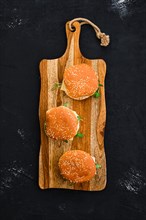 Overhead view of homemade burger with chicken cutlet on long wooden board