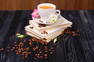 Cup of coffee on top of books pile with coffee beans and flowers scattered on the table