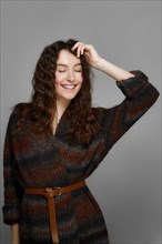 Happy fashion model in knitted woolen coat posing with closed eyes and smiling. perfect healthy skin. red lips