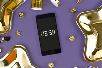 New Year Silvester celebration concept with smart phone with timer countdown to midnight between party items on purple background